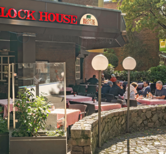BLOCK HOUSE Hamburg Volksdorf – Steakhouse mit Terrasse BLOCK HOUSE Hamburg Volksdorf mit Gästen vor dem Steakhouse und Sitzplätzen auf der Terrasse unter großen Bäumen