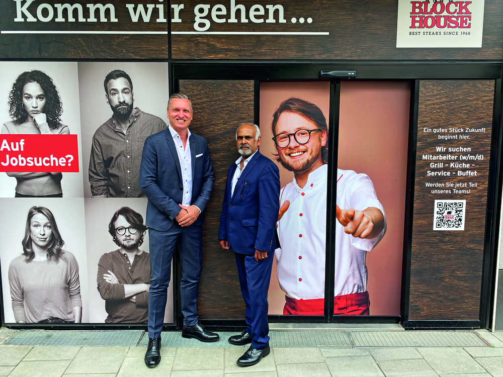 Zwei Herren in Anzügen stehen vor dem BLOCK HOUSE Restaurant München Rindermarkt mit Recruting-Werbung