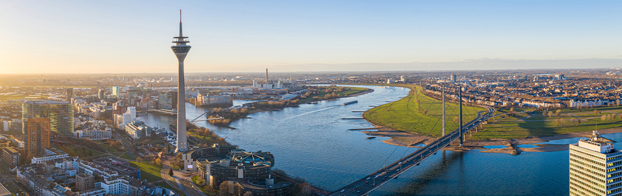 Panoramablick über Düsseldorf mit Rheinturm, Rhein und Rheinkniebrücke bei Sonnenuntergang.