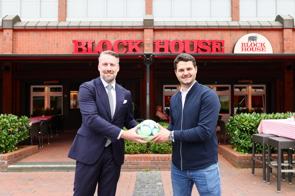 Zwei Männer vor dem BLOCK HOUSE Alstertal halten gemeinsam einen Fußball