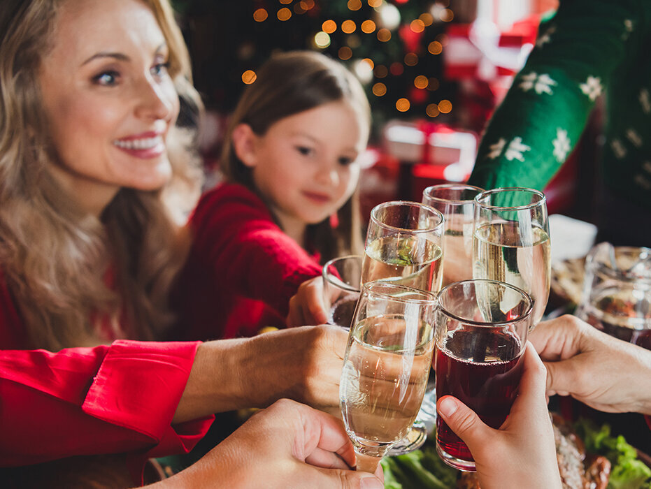 Weihnachtlich gekleidete Personen stoßen mit einem Sektglas an.