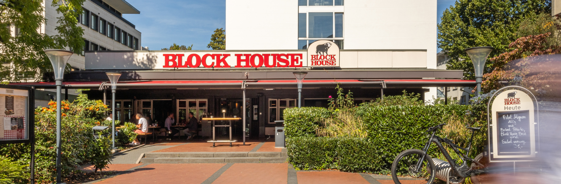 Außenansicht des BLOCK HOUSE Frankfurt Westend mit Terrasse, Eingang zum Steakhouse und Gästen im Außenbereich