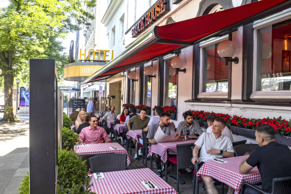 Terrasse des BLOCK HOUSE Hamburg Kirchenallee mit Gästen an Tischen mit rot-weiß karierten Tischdecken