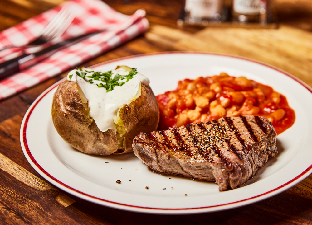 Steak, Ofenkartoffel und Gemüsebeilage liegen auf einem Teller in einem Block House