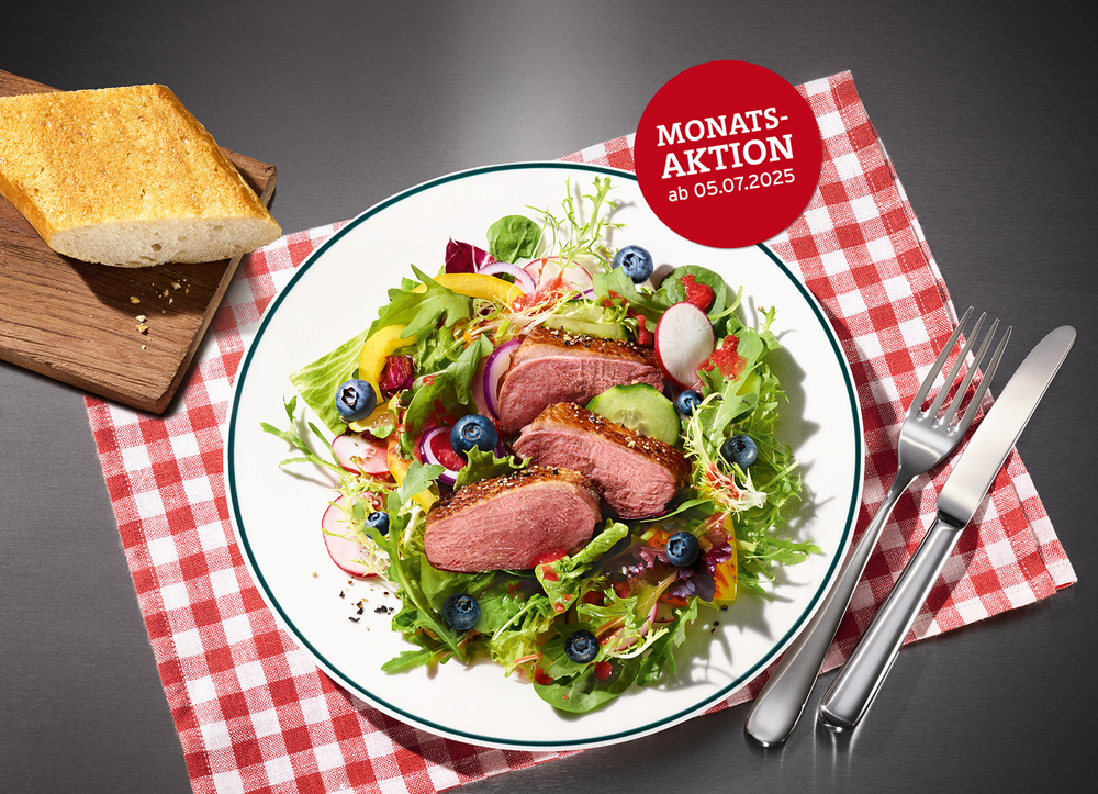 Ein Teller mit zart gebratener Flugentenbrust auf grünem Blattsalat, Blaubeeren, Radieschen und fruchtigem Dressing. Der Teller steht auf einem rot-weiß karierten Tuch, daneben liegt BLOCK HOUSE Brot auf einem Holzbrett.