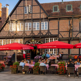 BLOCK HOUSE Hamburg Bergedorf Außenansicht des BLOCK HOUSE Hamburg Bergedorf mit gut besuchter Terrasse, roten Sonnenschirmen und historischem Fachwerkgebäude.
