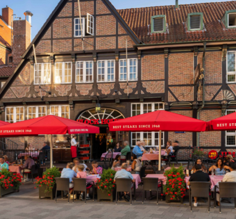 BLOCK HOUSE Hamburg Bergedorf Außenansicht des BLOCK HOUSE Hamburg Bergedorf mit gut besuchter Terrasse, roten Sonnenschirmen und historischem Fachwerkgebäude.