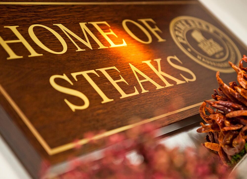 Blick von schräg unten auf ein Holzschild mit der Aufschrift "Home of Steaks"