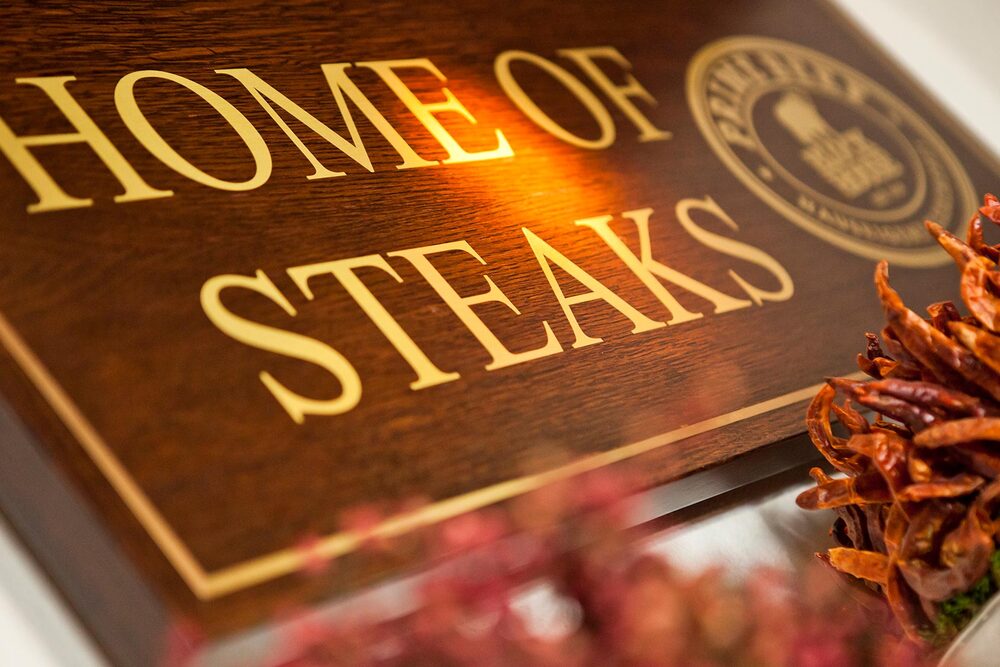 Blick von schräg unten auf ein Holzschild mit der Aufschrift "Home of Steaks"