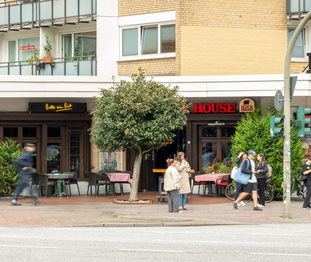 Außenansicht des BLOCK HOUSE Hamburg-Eppendorf mit Terrasse und Passanten an der Straße.