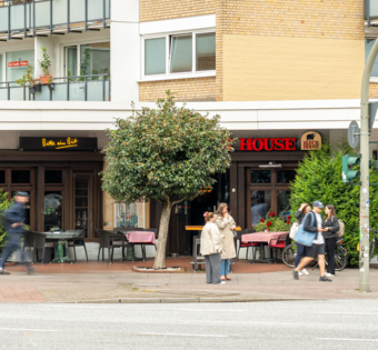 Außenansicht des BLOCK HOUSE Hamburg-Eppendorf mit Terrasse und Passanten an der Straße.