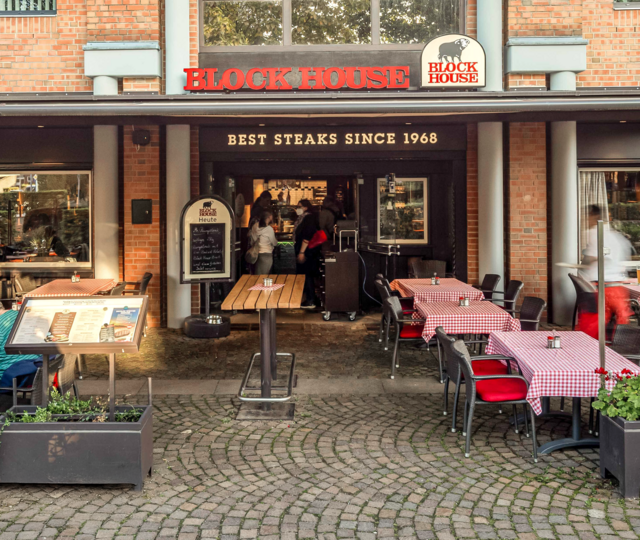 Terrasse des BLOCK HOUSE Ahrensburg mit Gästen an Tischen mit rot-weiß karierten Tischdecken vor dem Steakhouse