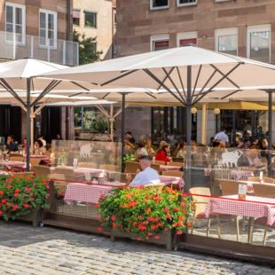 BLOCK HOUSE Nürnberg – Außenterrasse mit blühenden Geranien Speisende Gäste auf der sonnengeschützten Terrasse des BLOCK HOUSE Restaurants in Nürnberg
