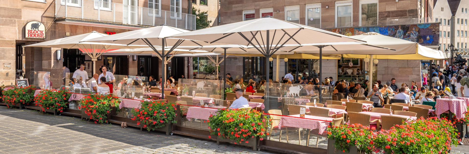 BLOCK HOUSE Nürnberg – Außenterrasse mit blühenden Geranien Speisende Gäste auf der sonnengeschützten Terrasse des BLOCK HOUSE Restaurants in Nürnberg