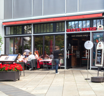 Außenansicht des BLOCK HOUSE Stuttgart Königstraße mit Terrasse und Gästen vor dem Restaurant.