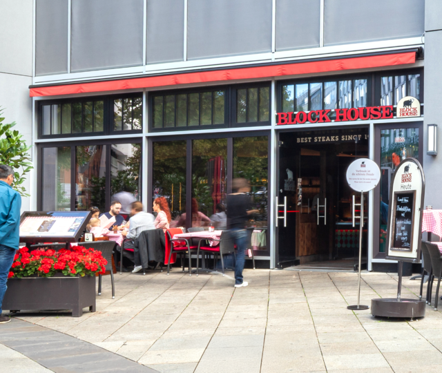 Außenansicht des BLOCK HOUSE Stuttgart Königstraße mit Terrasse und Gästen vor dem Restaurant.