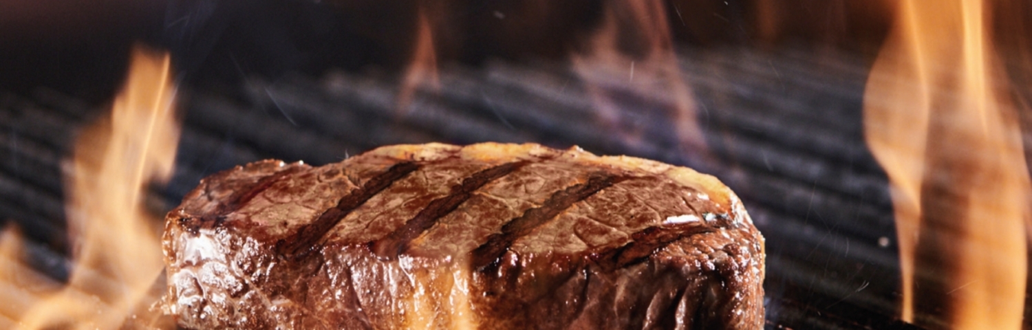 Ein Steak liegt auf einem Grill, umgeben von Flammen