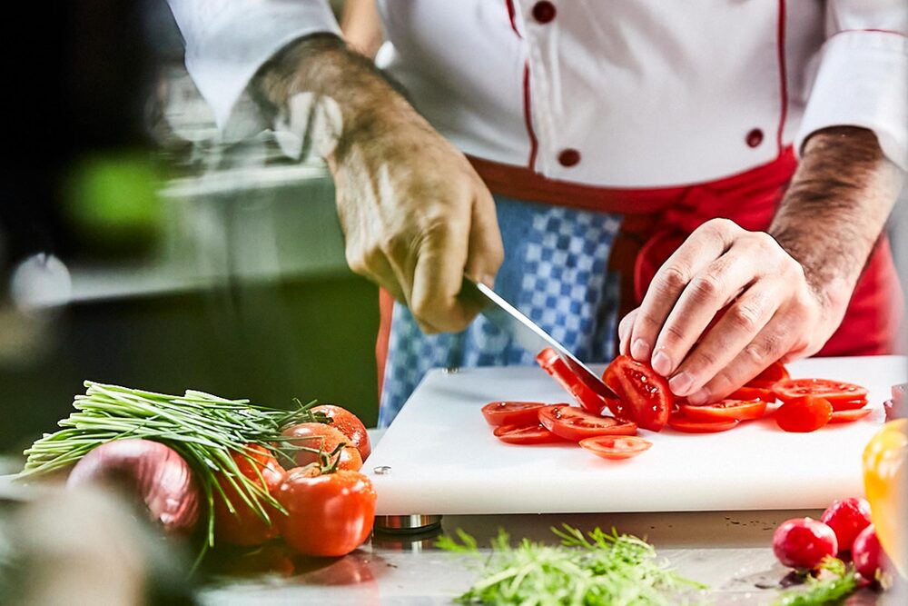 Frische Zubereitung in der Küche Ein Koch im Restaurant schneidet eine frische Tomate in Scheiben