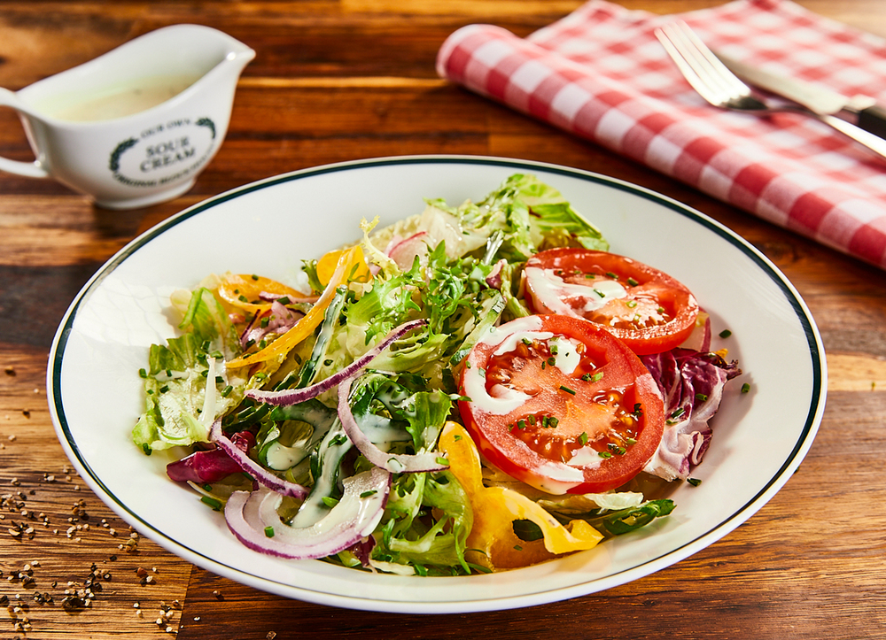 Salat mit Tomaten, Paprika, Zwiebeln und American Dressing auf einem Teller im Block House