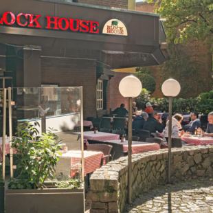 BLOCK HOUSE Hamburg Volksdorf mit Gästen vor dem Steakhouse und Sitzplätzen auf der Terrasse unter großen Bäumen