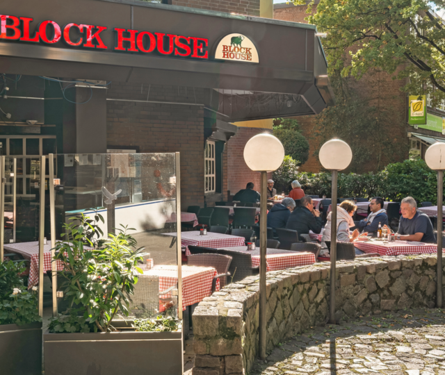 BLOCK HOUSE Hamburg Volksdorf mit Gästen vor dem Steakhouse und Sitzplätzen auf der Terrasse unter großen Bäumen