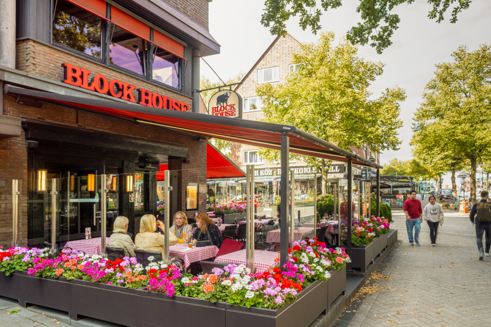 Terrasse des BLOCK HOUSE Hamburg Barmbek mit Gästen, rot-weiß karierten Tischdecken und Blumen vor dem Steakhouse