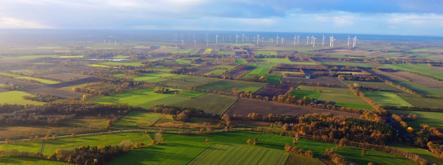 Vogelperspektive auf grüne Felder im Hintergrund weiße Windräder