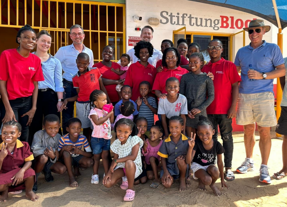 Eine Gruppe von Kindern und Erwachsenen steht fröhlich vor einem Kindergarten in Namibia.