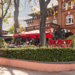 BLOCK HOUSE Hamburg Othmarschen mit Terrasse, roten Sonnenschirmen und Gästen vor dem Steakhouse im grünen Umfeld