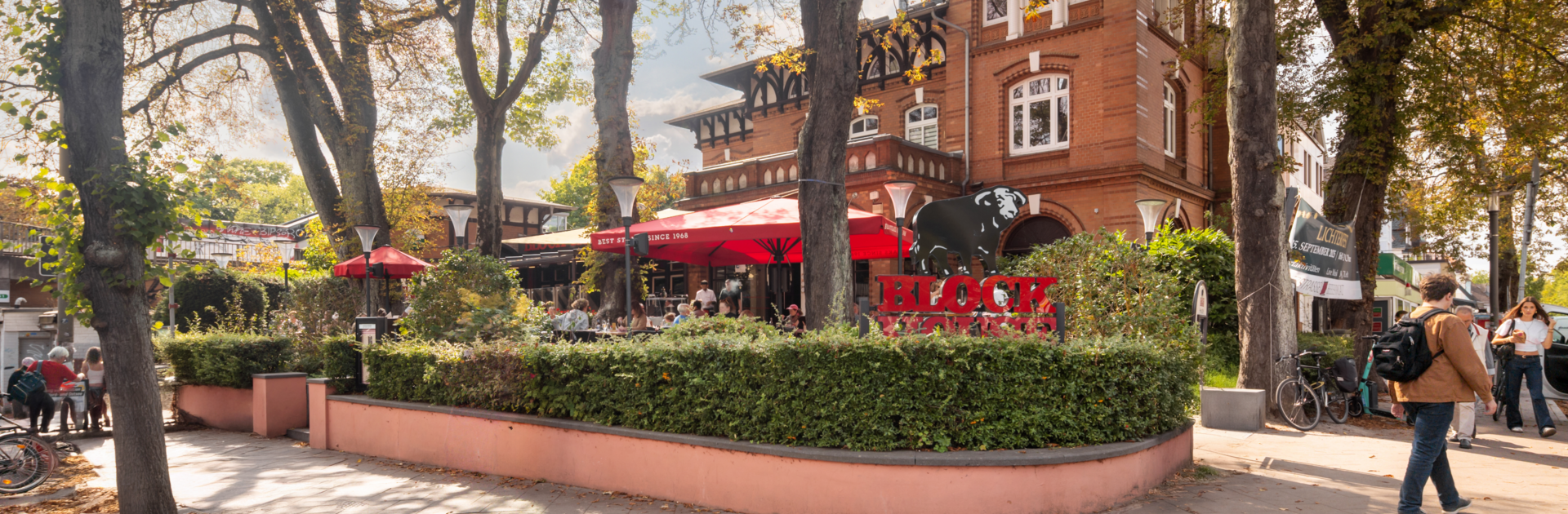 BLOCK HOUSE Hamburg Othmarschen mit Terrasse, roten Sonnenschirmen und Gästen vor dem Steakhouse im grünen Umfeld