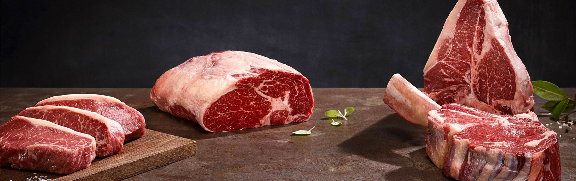 Rohe Steaks vom Rind vor schwarzem Hintergrund, auf einer braunen Steinoberfläche