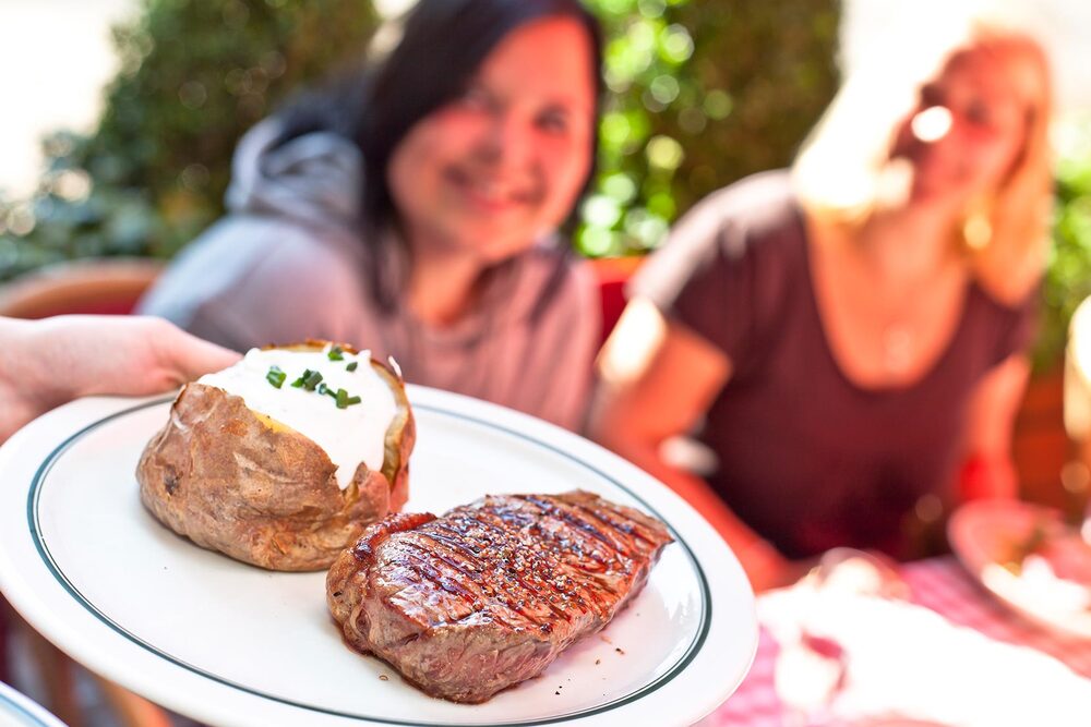 BLOCK HOUSE Steak und Ofenkartoffel Steak und eine gefüllte Ofenkartoffel werden auf einem Teller serviert