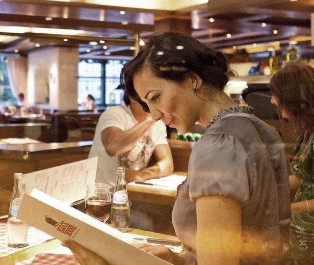 Frau liest BLOCK HOUSE Speisekarte an einem Tisch mit mehreren Menschen in einem BLOCK HOUSE Restaurant