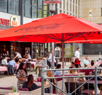 Außenansicht des BLOCK HOUSE Essen mit großer Terrasse, roten Sonnenschirmen und Gästen im Außenbereich.
