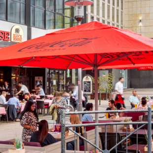 BLOCK HOUSE Essen Außenansicht des BLOCK HOUSE Essen mit großer Terrasse, roten Sonnenschirmen und Gästen im Außenbereich.