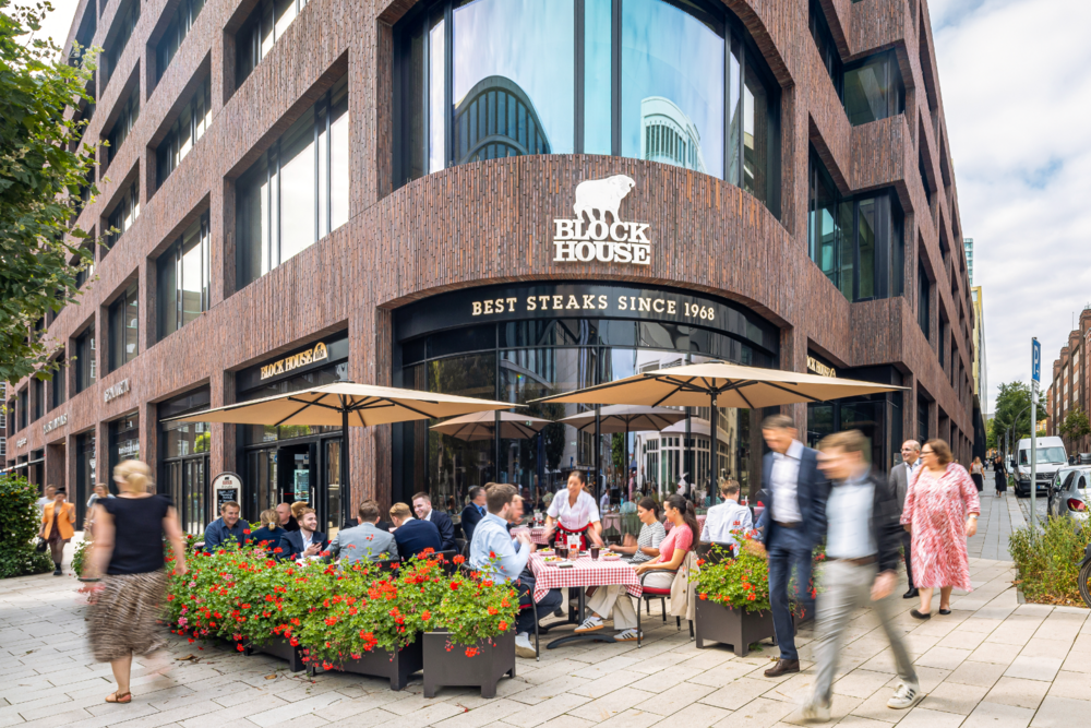 BLOCK HOUSE Deutschlandhaus Außenansicht des BLOCK HOUSE Deutschlandhaus mit Terrasse und Gästen vor dem Restaurant.