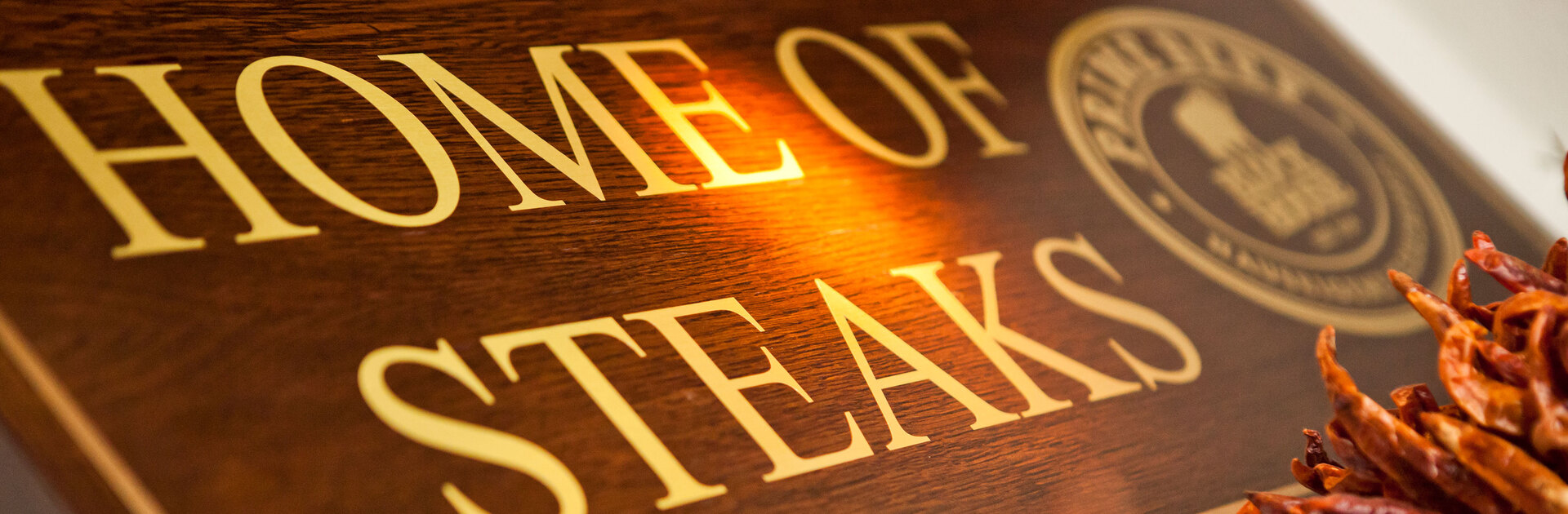 Blick von schräg unten auf ein Holzschild mit der Aufschrift "Home of Steaks"