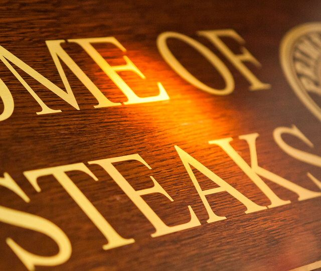 Blick von schräg unten auf ein Holzschild mit der Aufschrift "Home of Steaks"