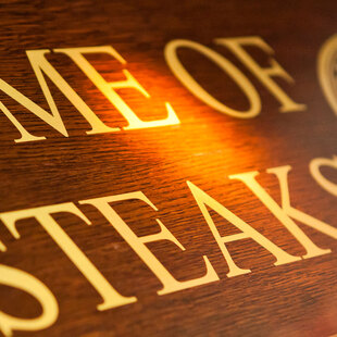 Blick von schräg unten auf ein Holzschild mit der Aufschrift "Home of Steaks"