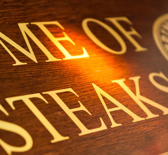 Blick von schräg unten auf ein Holzschild mit der Aufschrift "Home of Steaks"