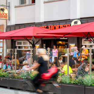 Terrasse des BLOCK HOUSE Hannover Am Kröpcke mit Gästen unter roten Sonnenschirmen in der Fußgängerzone der Innenstadt