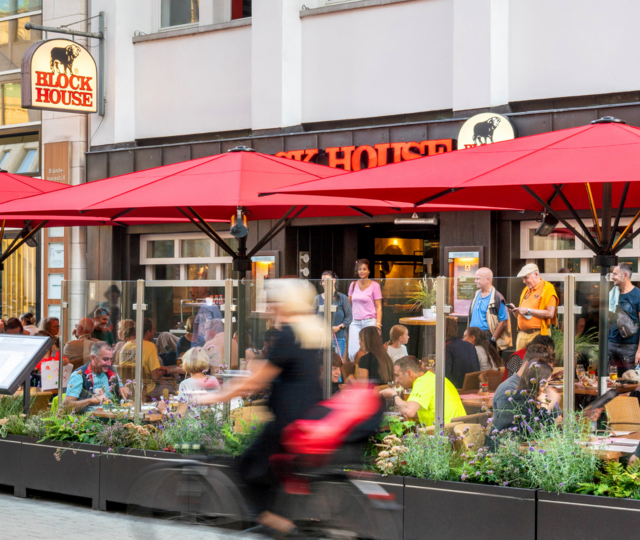 BLOCK HOUSE Hannover Am Kröpcke – Steakhouse mit Terrasse Terrasse des BLOCK HOUSE Hannover Am Kröpcke mit Gästen unter roten Sonnenschirmen in der Fußgängerzone der Innenstadt