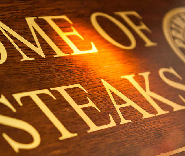 Blick von schräg unten auf ein Holzschild mit der Aufschrift "Home of Steaks"