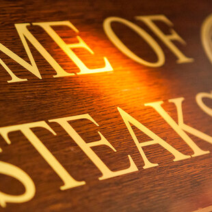 Blick von schräg unten auf ein Holzschild mit der Aufschrift "Home of Steaks"