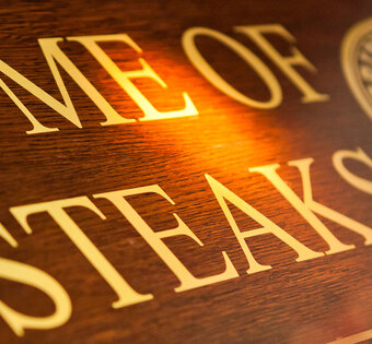 Blick von schräg unten auf ein Holzschild mit der Aufschrift "Home of Steaks"