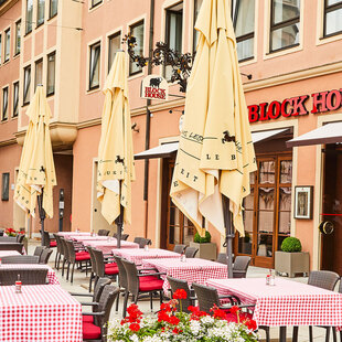 Außenansicht des BLOCK HOUSE Restaurants in Augsburg: eine große, hölzerne Fensterfront, davor viele Sitzgelegenheiten auf der Terrasse, die sich direkt auf dem Ulrichsplatz befindet.