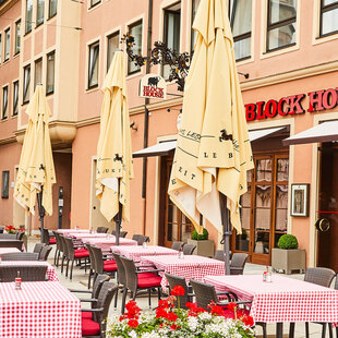 BLOCK HOUSE Restaurant Augsburg Außenansicht des BLOCK HOUSE Restaurants in Augsburg: eine große, hölzerne Fensterfront, davor viele Sitzgelegenheiten auf der Terrasse, die sich direkt auf dem Ulrichsplatz befindet.