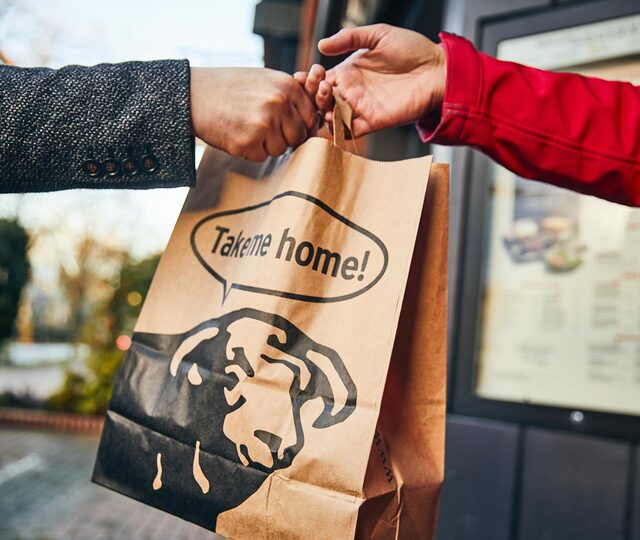 BLOCK HOUSE Mitarbeiter übergibt eine Takeaway Papiertüte mit der Aufschrift „Take me home!“ 