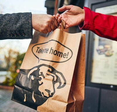 BLOCK HOUSE Mitarbeiter übergibt eine Takeaway Papiertüte mit der Aufschrift „Take me home!“ 