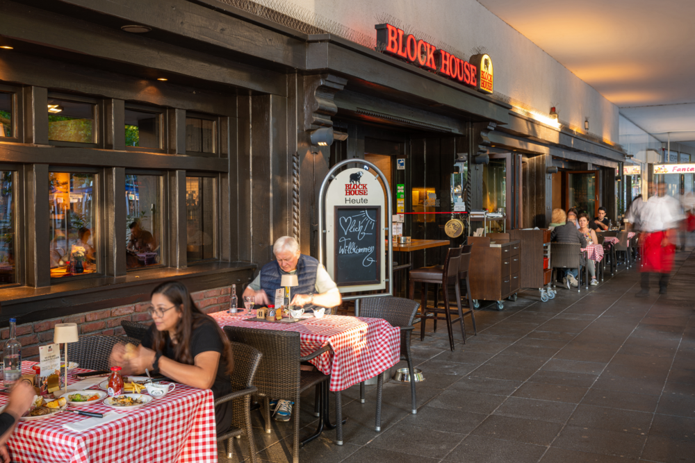 BLOCK HOUSE Hannover Am Aegi mit Gästen an Tischen mit rot-weiß karierten Tischdecken vor dem Steakhouse